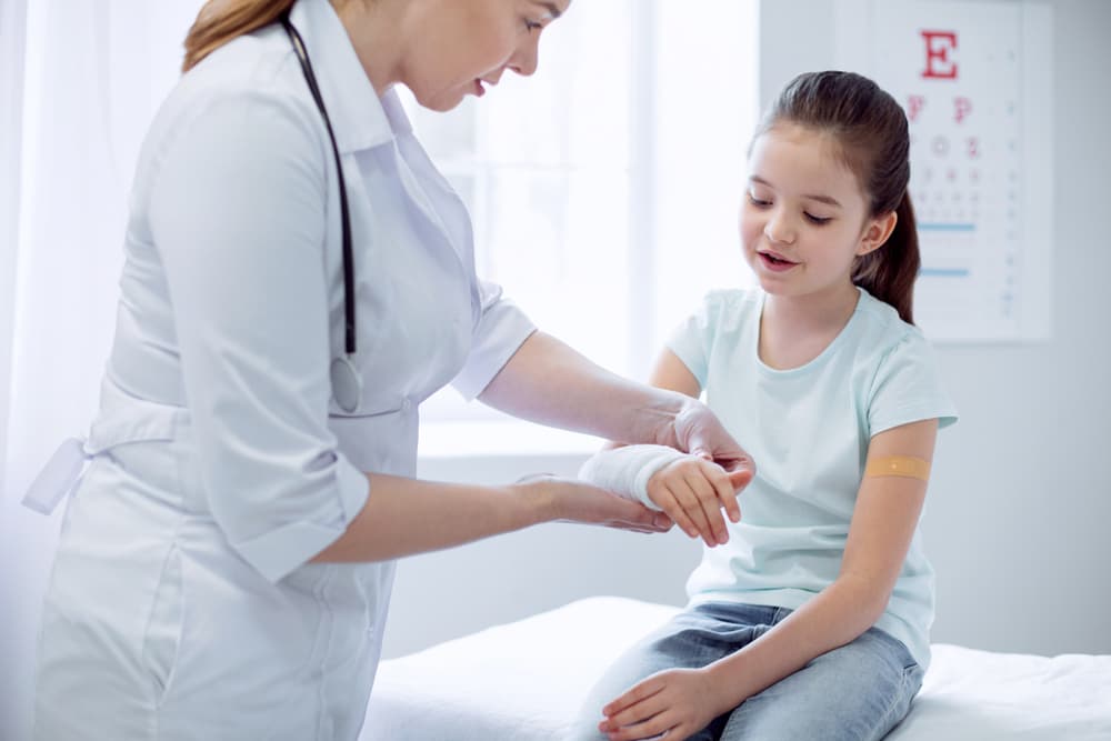 A cute girl has encountered a broken arm, and a female doctor is standing by, skillfully applying a plaster cast to aid in the healing process.